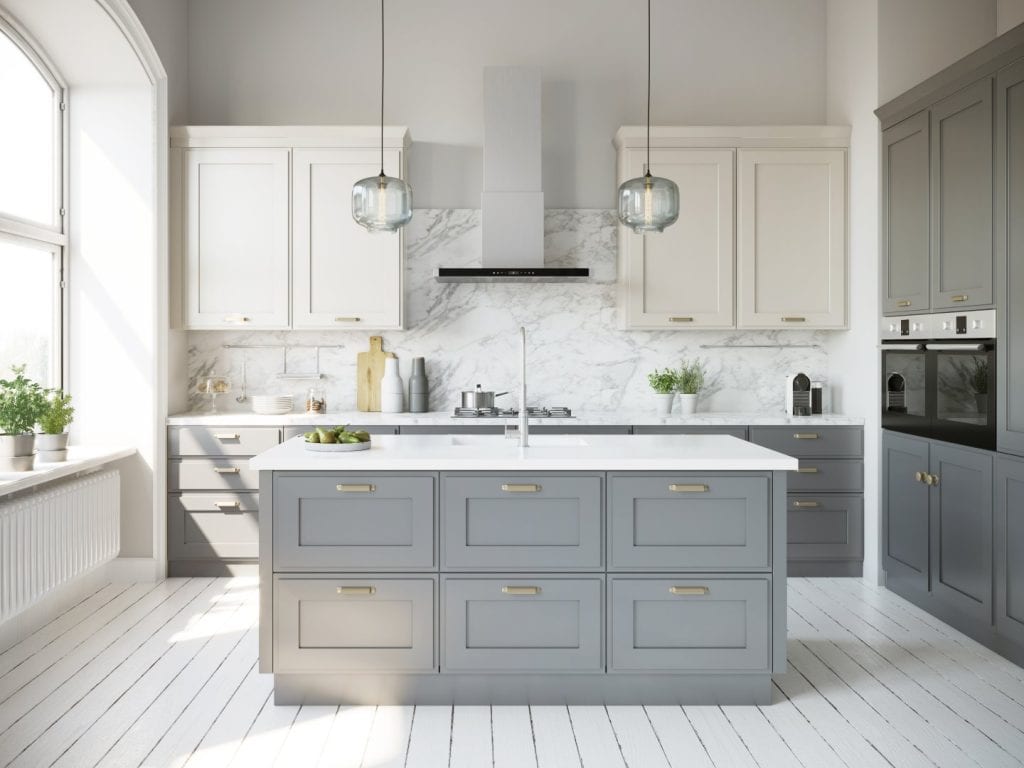 A bright, modern kitchen by a top general contractor in Contra Costa & Alameda County, featuring gray and white cabinets, a marble island, pendant lights, built-in ovens, and potted plants. Sunlight streams through the large window.