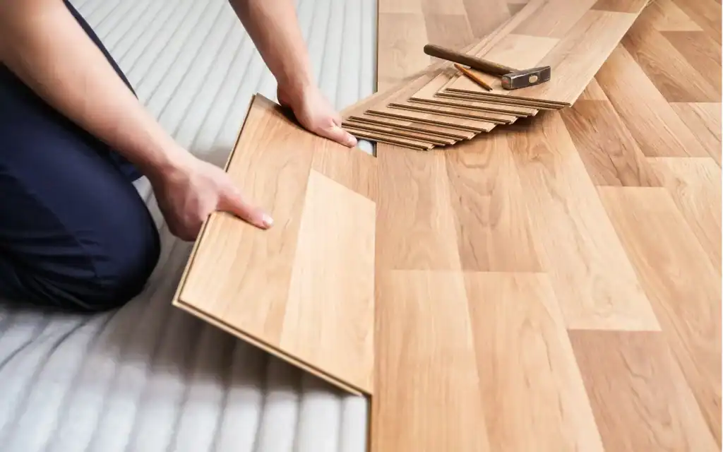 A general contractor in Contra Costa & Alameda County, CA, installs wooden laminate flooring, carefully aligning planks on a foam underlay with a hammer nearby.