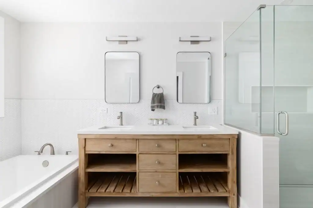 Modern bathroom in CA featuring a wooden double-sink vanity, two rectangular mirrors, wall lights, a glass shower enclosure, and a white bathtub. Designed by a general contractor Contra Costa & Alameda County for minimalist style and clean lines.