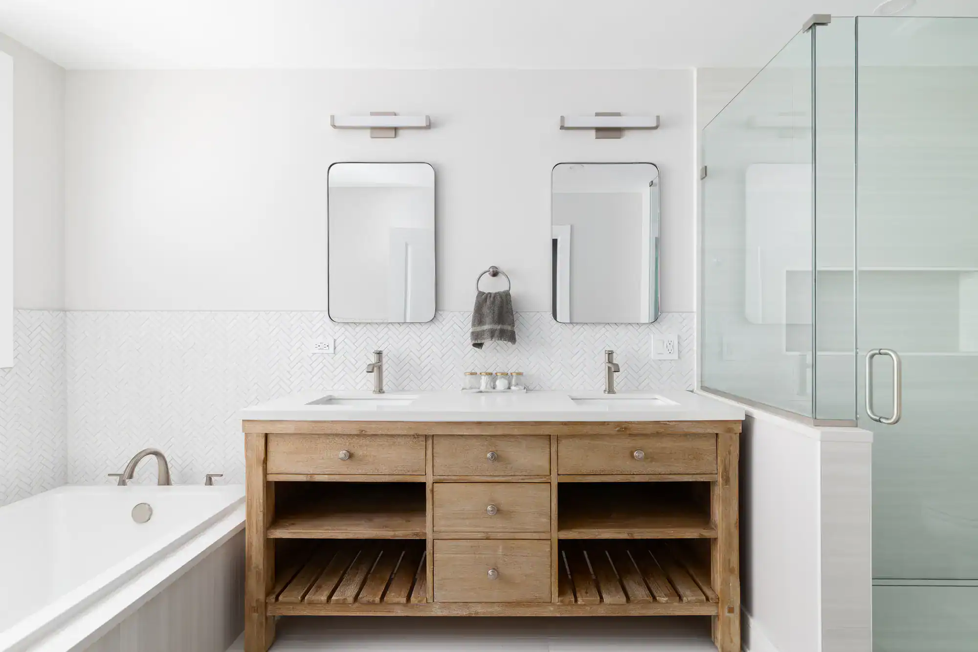 Modern bathroom with a wooden double-sink vanity, two rectangular mirrors, and a glass-enclosed shower on the right. Bright and minimalistic, it showcases the quality of a general contractor Contra Costa & Alameda County, CA.