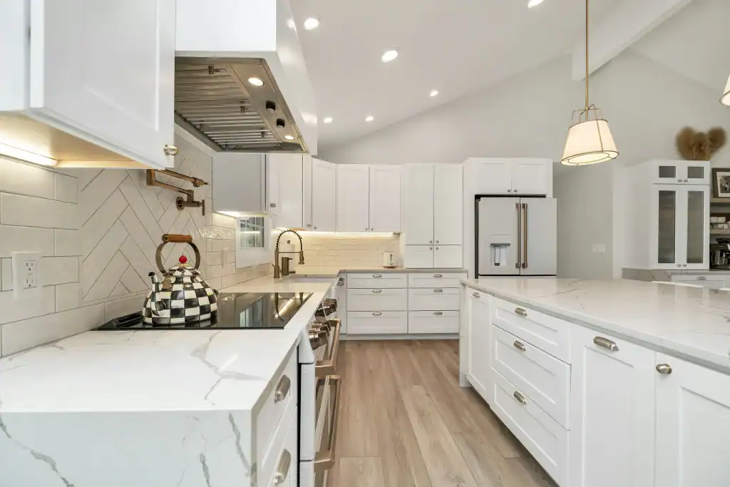 Modern white kitchen with marble countertops, white cabinets, stainless steel appliances, a checkered teapot on the stove, wood flooring, pendant lighting, and a bright, clean, and spacious layout.